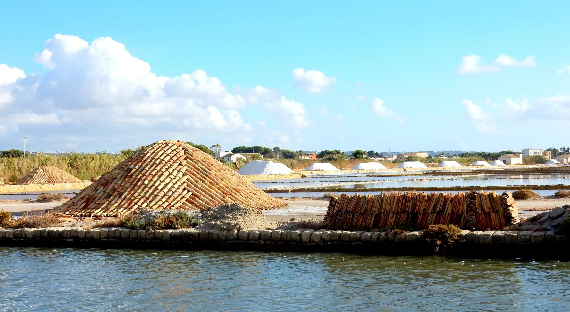 Salt pans at Trapani with a windmill and white heaps of salt by the sea.